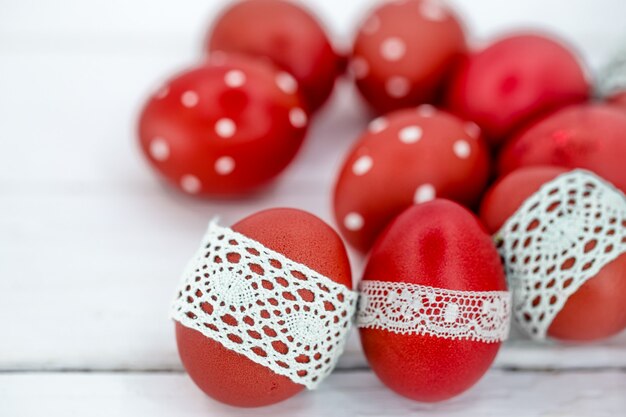 Ovos de Páscoa vermelhos em fita de renda branca amarrada, close-up, deitado sobre uma madeira branca