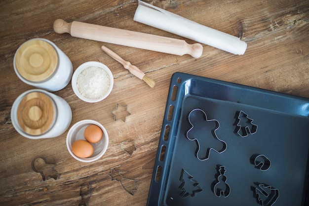 Ovos, farinha, rolo e formulários para biscoitos na bandeja de gotejamento