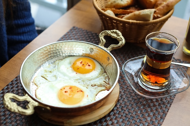 Ovos fritos na frigideira na tábua de madeira chá no pão armudy