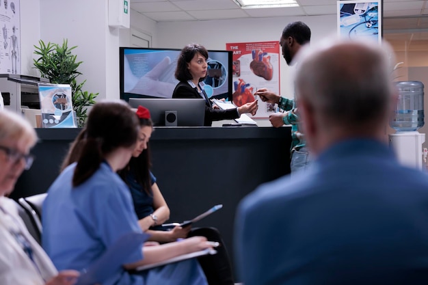 Paciente afro-americano assinando o formulário de admissão em clínica privada na recepção do hospital. Recepcionista do centro de saúde segurando a prancheta para o homem assinar antes da consulta médica.