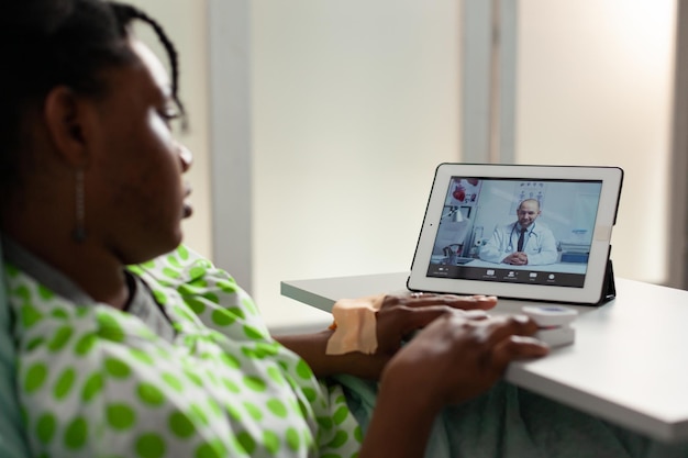 Foto grátis paciente afro-americano doente, deitado na cama, discutindo o tratamento medicamentoso com o médico remoto durante a conferência de videochamada online. chamada tele-saúde na tela do tablet