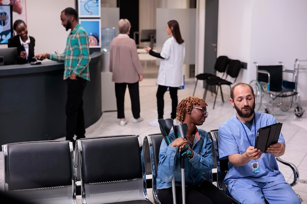 Foto grátis paciente afro-americano e enfermeira olhando para tablet para encontrar diagnóstico de doença em dispositivo digital, sofrendo de deficiência física na área de espera. mulher e especialista em lobby hospitalar.