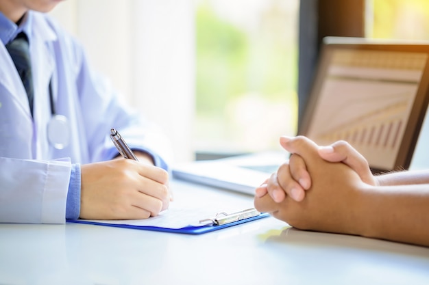 Paciente de consulta do homem do doutor ao encher acima um formulário de candidatura na mesa no hospital.