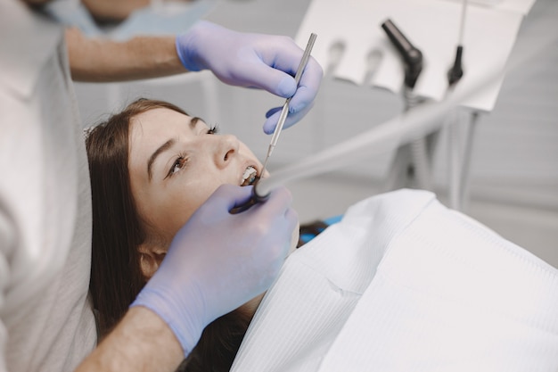 Paciente do sexo feminino com aparelho ortodôntico tem exame odontológico no consultório dentista. Mulher vestindo roupas brancas