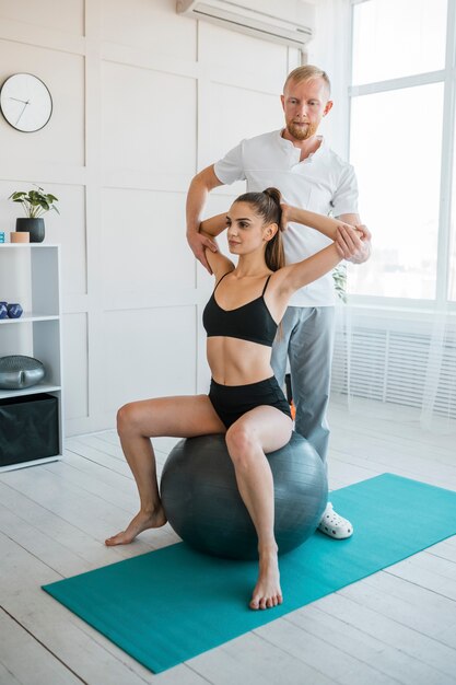 Paciente do sexo feminino fazendo exercícios com bola e fisioterapeuta masculino