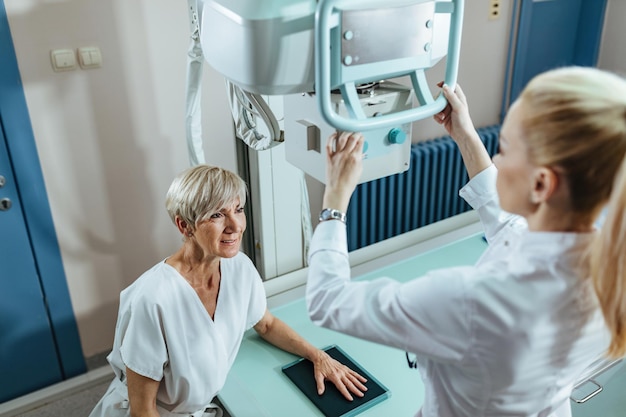 Paciente do sexo feminino maduro e técnico médico durante o exame de raio-x manual na clínica