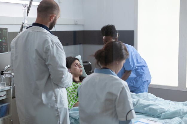 Paciente internado no hospital se recuperando na cama, recebendo cuidados de saúde profissionais de uma enfermeira experiente enquanto os médicos examinam os sintomas. equipe de médicos consultando a doença da mulher durante as rodadas.