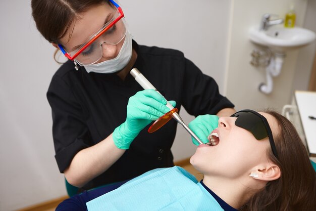 Paciente jovem com óculos de proteção e dentes tratados por higienista usando fotopolimerizador