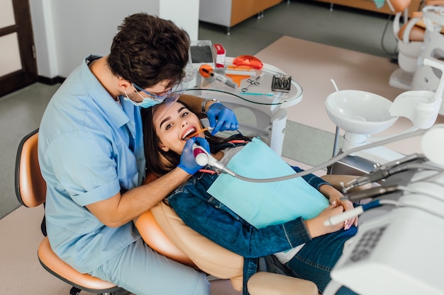 Paciente jovem do sexo feminino com a boca aberta, examinando a inspeção odontológica no consultório dentista.