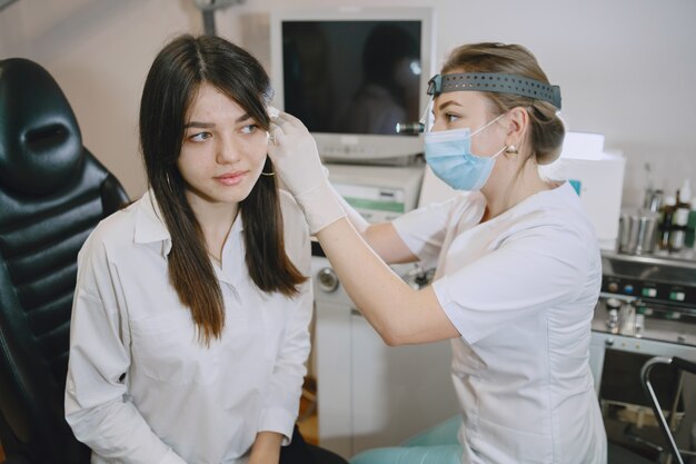 Paciente mulher no consultório médico. Doutor em máscara médica. Lor verifica as orelhas da mulher.