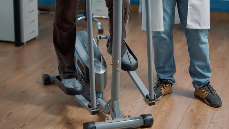 Foto grátis paciente sênior fazendo exercício de fisioterapia na bicicleta de bem-estar para curar lesões físicas na consulta de reabilitação, recebendo apoio do médico do sexo masculino. medicina alternativa.