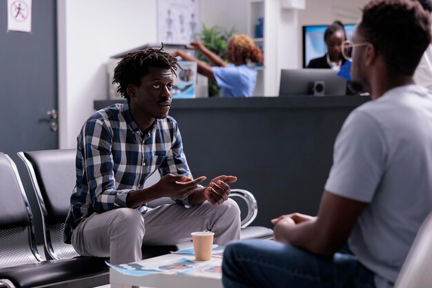 Pacientes afro-americanos esperando no saguão para comparecer ao exame médico, falando sobre suporte de saúde antes da consulta. Adultos com doença esperando para receber medicamentos e tratamento.