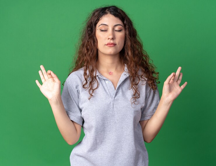 Foto grátis pacífica jovem bonita caucasiana meditando com os olhos fechados, isolada na parede verde