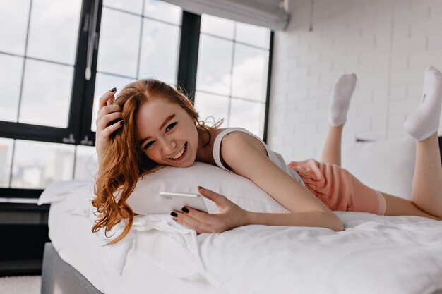 Pacífica menina europeia deitada na cama. Foto interna de mulher de gengibre em meias brancas, passando a manhã em casa.