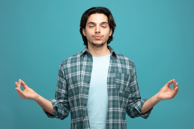 pacífico jovem bonito meditando com os olhos fechados, isolados no fundo azul