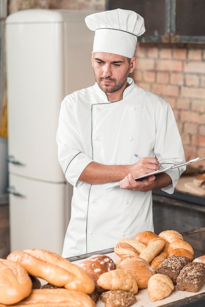 Padeiro, em, uniforme, fazendo notas, de, sortido, assado, pão