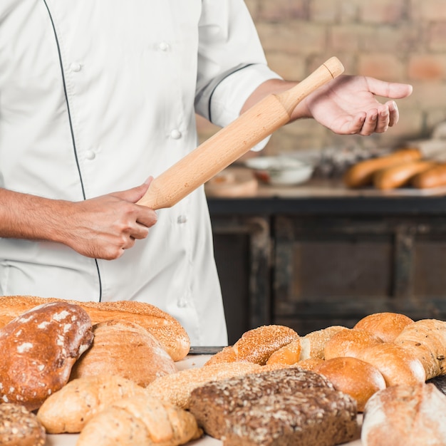 Padeiro masculino segurando o rolo de madeira com variedade de pães na mesa