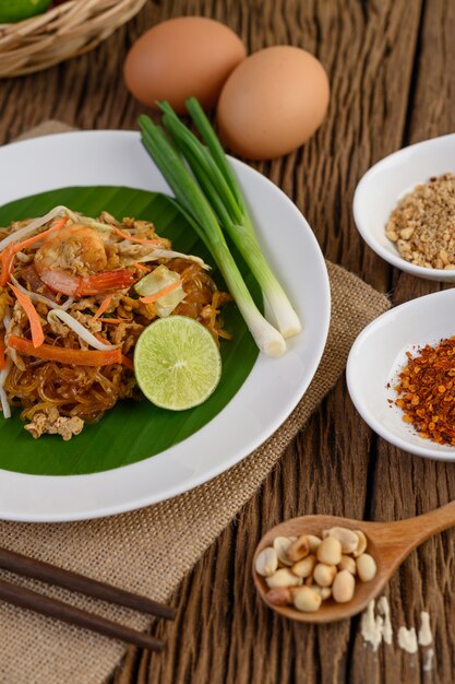 Padthai camarão em um prato branco com limão e ovos na mesa de madeira.