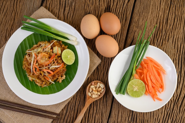 Foto grátis padthai camarão em um prato branco com limão e ovos na mesa de madeira.