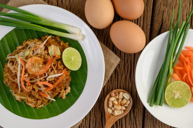 Padthai camarão em um prato branco com limão e ovos na mesa de madeira.
