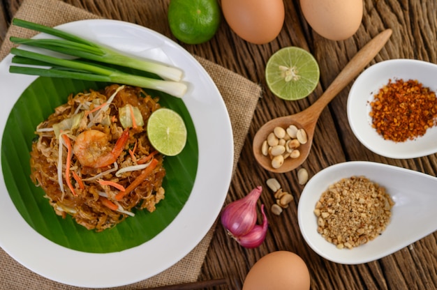 Padthai camarão em uma tigela preta com ovos, cebolinha e tempero na mesa de madeira.