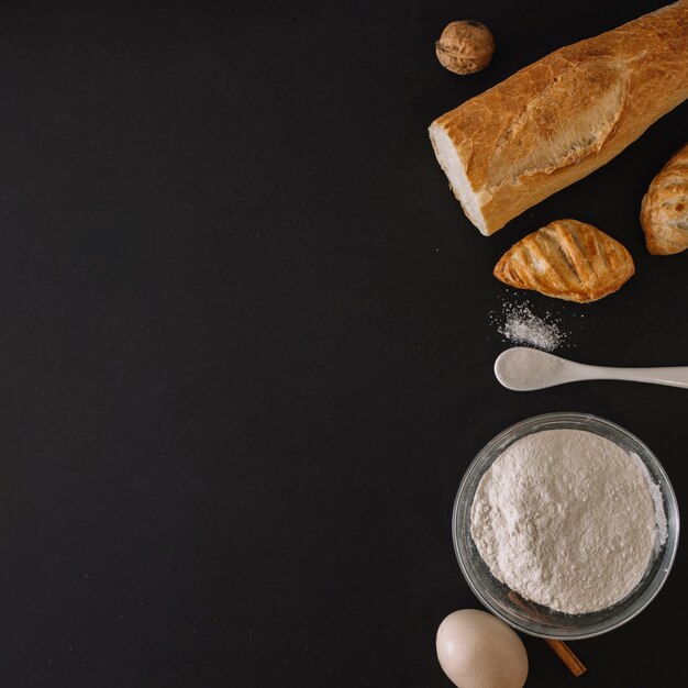 Pães assados; farinha; ovo e noz em fundo preto