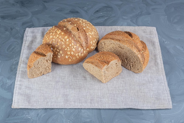 Pães inteiros e fatiados empacotados em uma toalha na mesa de mármore.