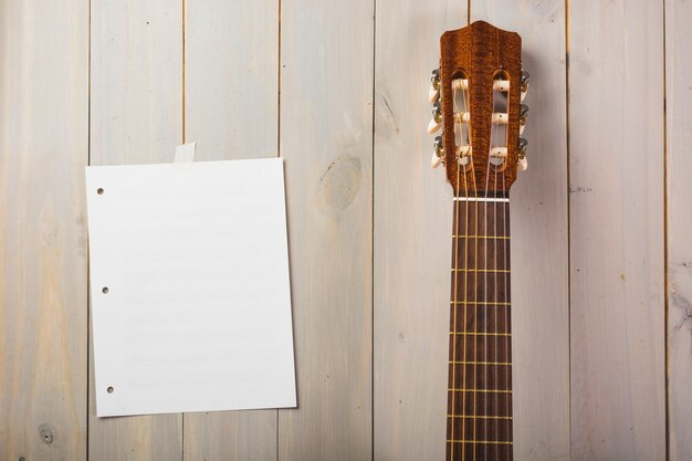 Página musical em branco preso na parede de madeira com cabeça de guitarra