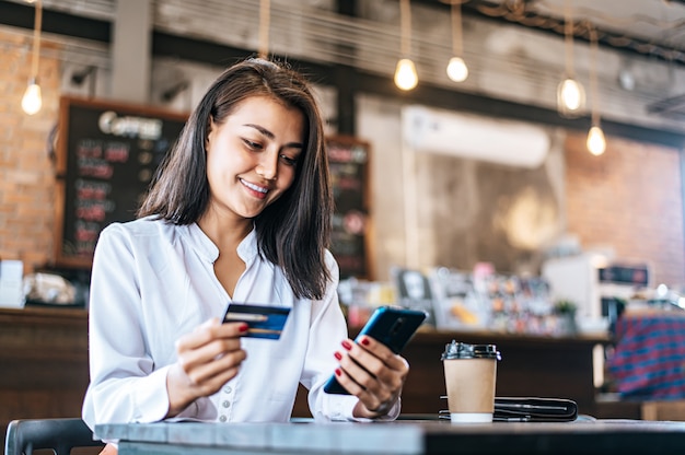 Pague as mercadorias com cartão de crédito através de um smartphone em uma cafeteria.