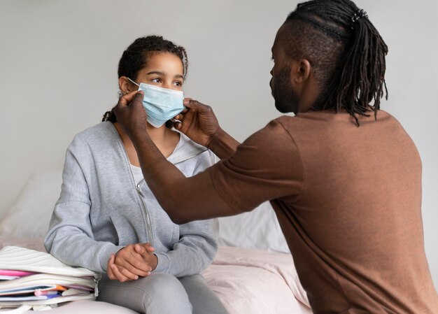 Pai ajudando a filha a colocar a máscara médica