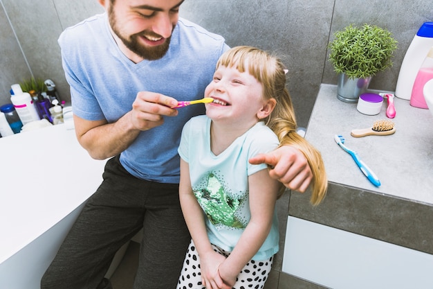 Foto grátis pai alegre, ajudando a filha a escovar os dentes