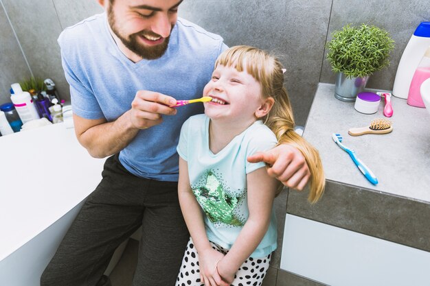 Pai alegre, ajudando a filha a escovar os dentes