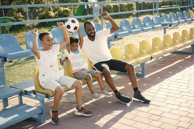 Pai animado e dois filhos assistindo a um jogo de futebol no estádio e torcendo pela vitória