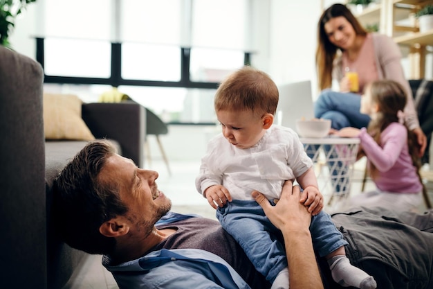 Pai carinhoso passando tempo com seu filho bebê em casa Mãe e filha estão se comunicando em segundo plano