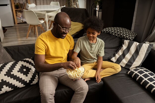 Pai comendo pipoca com filho no sofá em casa