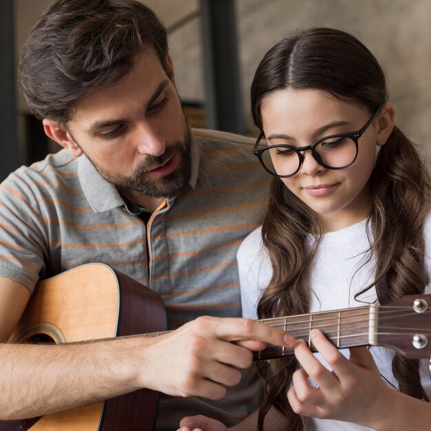 Pai de alto ângulo, ensinando a menina a tocar violão