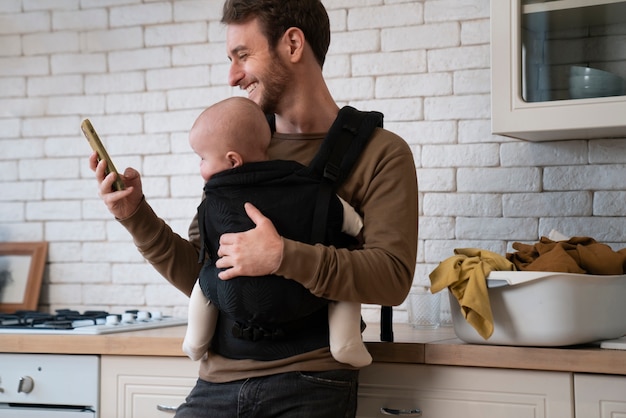 Foto grátis pai de tiro médio segurando bebê e telefone