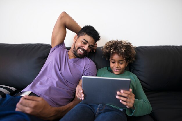 Pai e filha brincando de tablet no sofá da sala