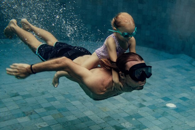 Pai e filha nadando juntos na piscina