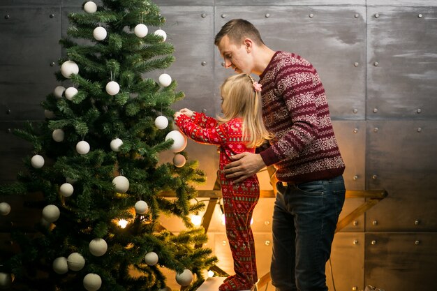 Pai e filha pendurados brinquedos em uma árvore de Natal
