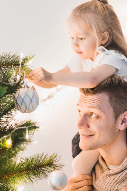 Foto grátis pai e filha que decoram a árvore de natal iluminada