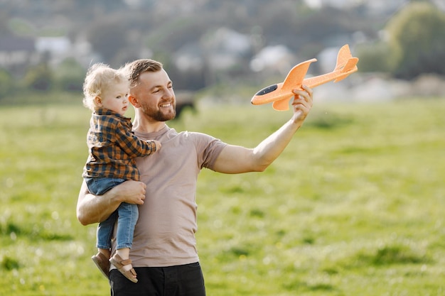 Pai e filho brincando com um avião de brinquedo e se divertindo no parque de verão ao ar livre. garoto curly vestindo jeans e camisa xadrez