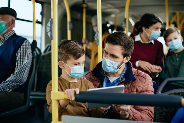 Pai e filho com máscaras usando o touchpad enquanto viajam de ônibus