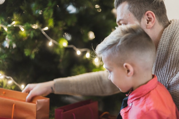 Pai e filho com saco na frente da árvore de natal