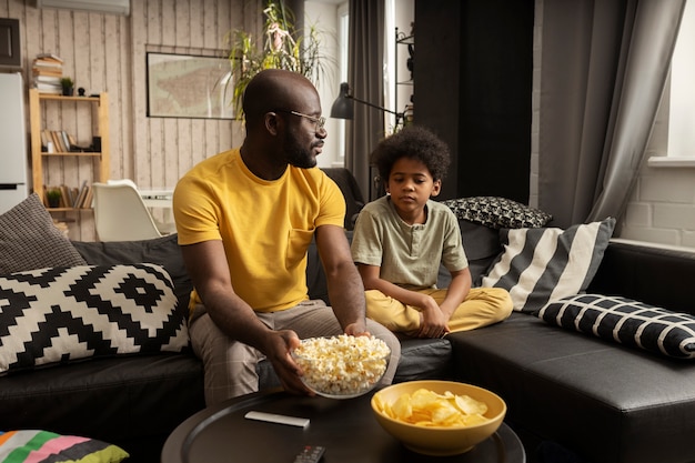 Pai e filho comendo pipoca e batata frita juntos no sofá