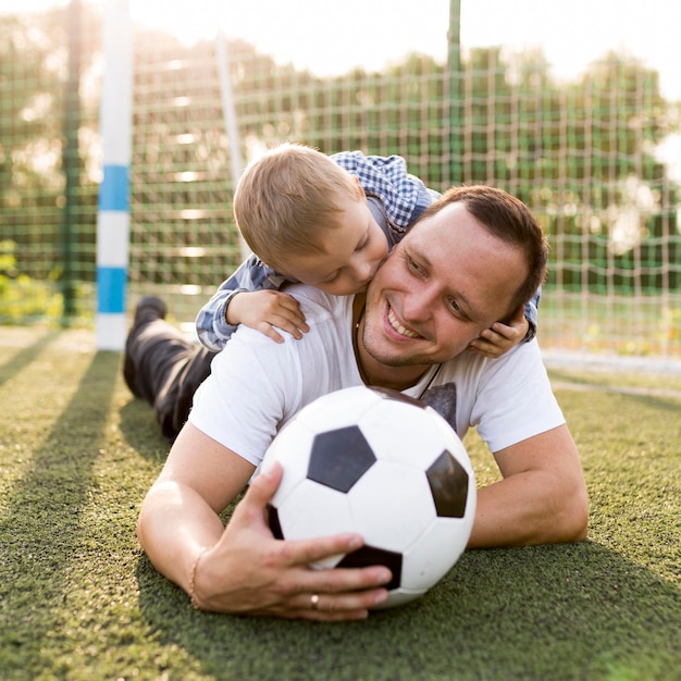 Foto grátis pai e filho descansando no campo de futebol