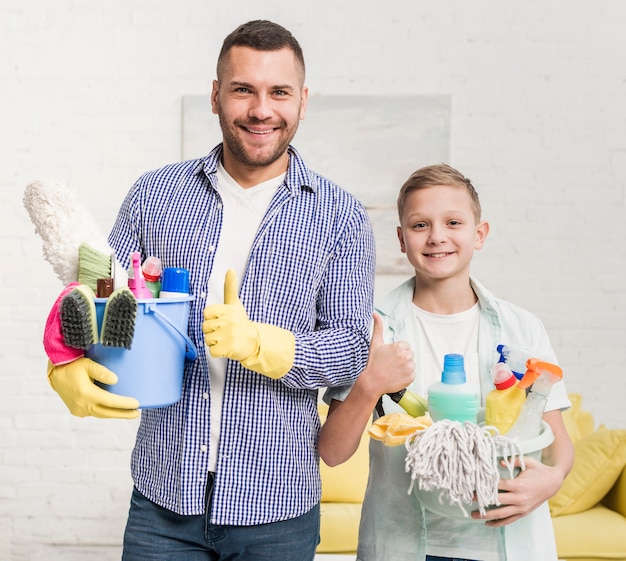 Pai e filho desistindo polegares enquanto segura produtos de limpeza