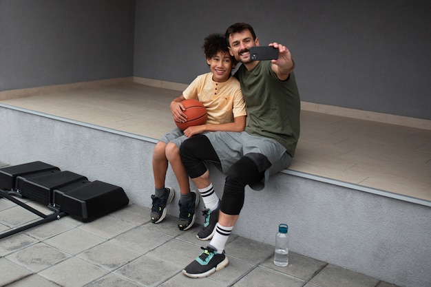 Foto grátis pai e filho tirando selfie no quintal enquanto jogavam basquete