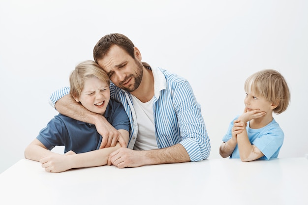 Pai e filhos escondendo segredo desagradável do menino mais novo. Retrato de pai e filho tristes e infelizes se abraçando e chorando