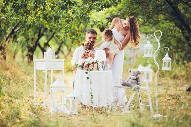 Pai e mãe com a filha no meio do campo com mesa e cadeiras brancas